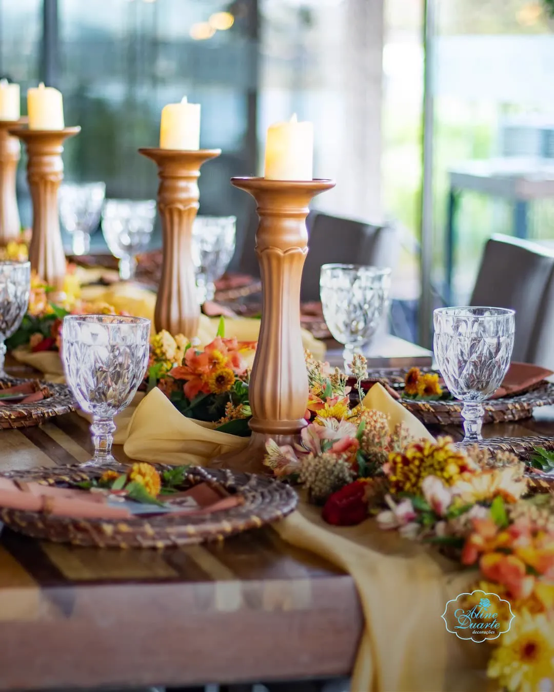 Mesa posta com castiçais de madeira, taças e flores